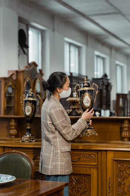 The image depicts an antique wooden sideboard with ornate detailing, placed against a light-colored wall inside a home. On top of the sideboard are various decorative objects including a table lamp wi